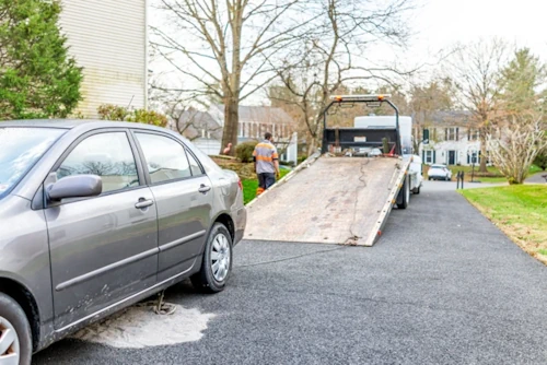 A car on a driveway being loaded onto a trailer for removal