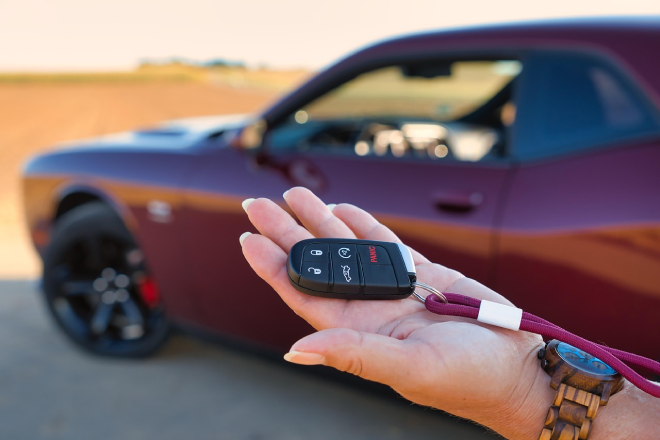 A person holds car keys in the palm of their hand in front of a red car