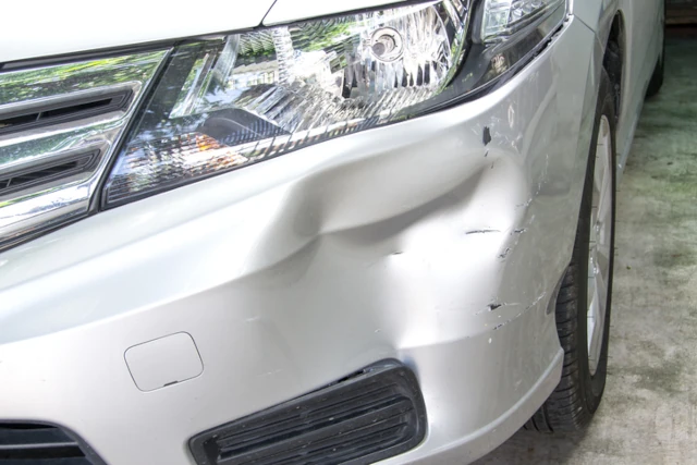 Close up of white car with dented fender